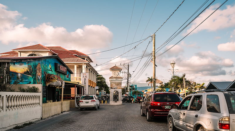 A street in a coastal Belizean town, with the town clock tower, painted murals and taxis at the kerb