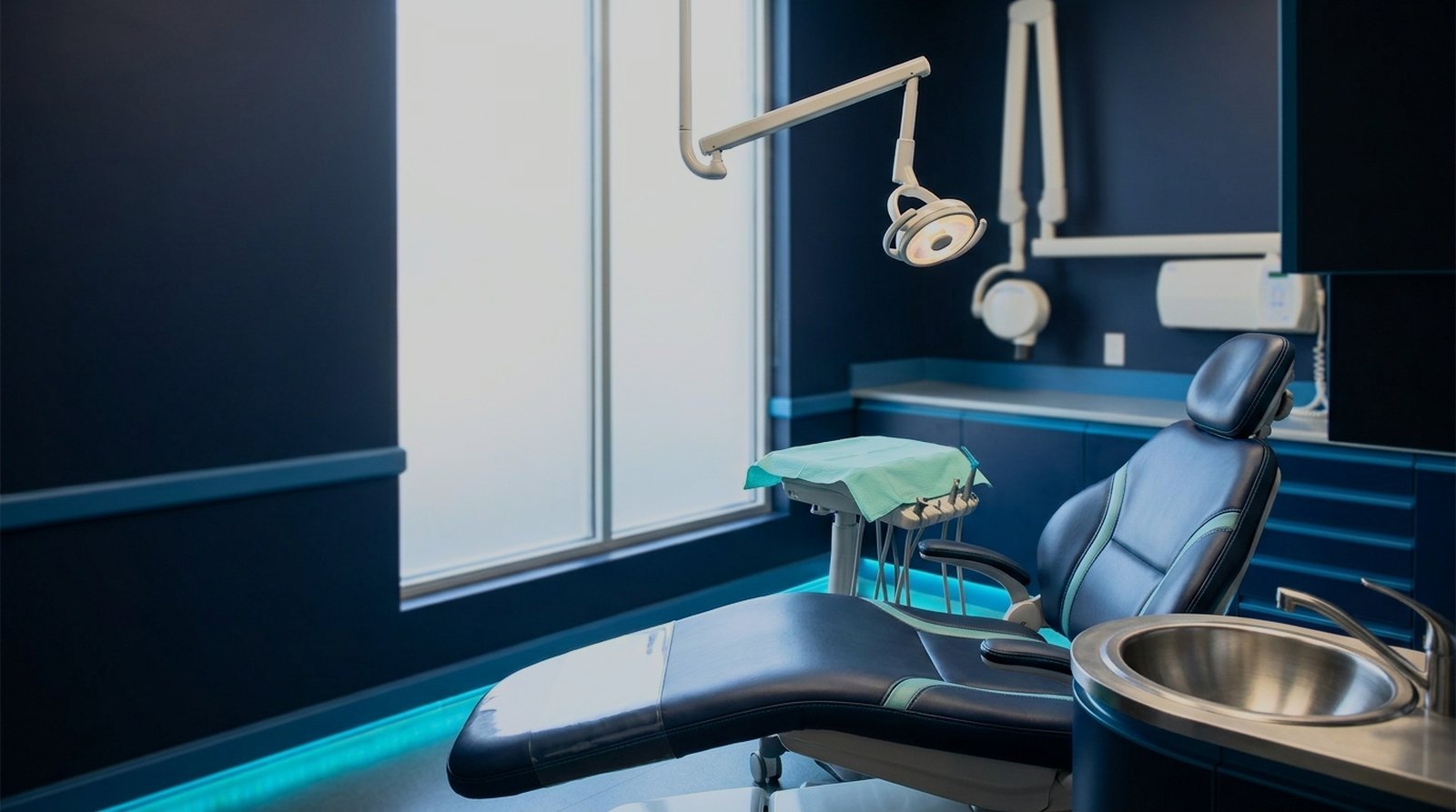 Empty dental operatory in early morning light with a clean chair and covered instrument tray