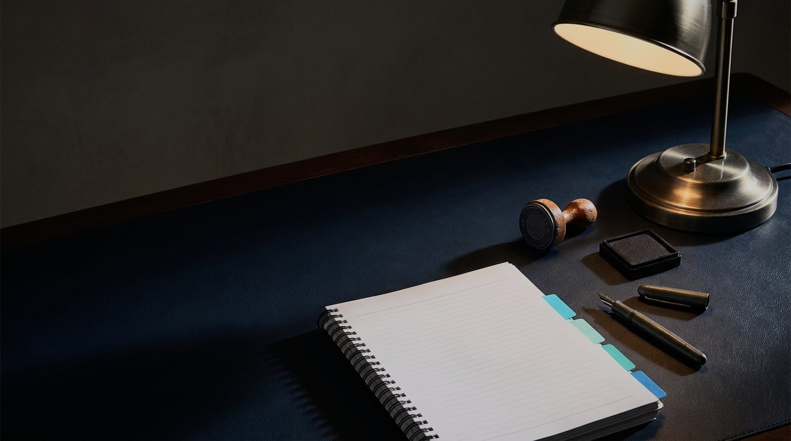 Procurement desk under a lamp with a tabbed comb bound document, a stamp and an ink pad
